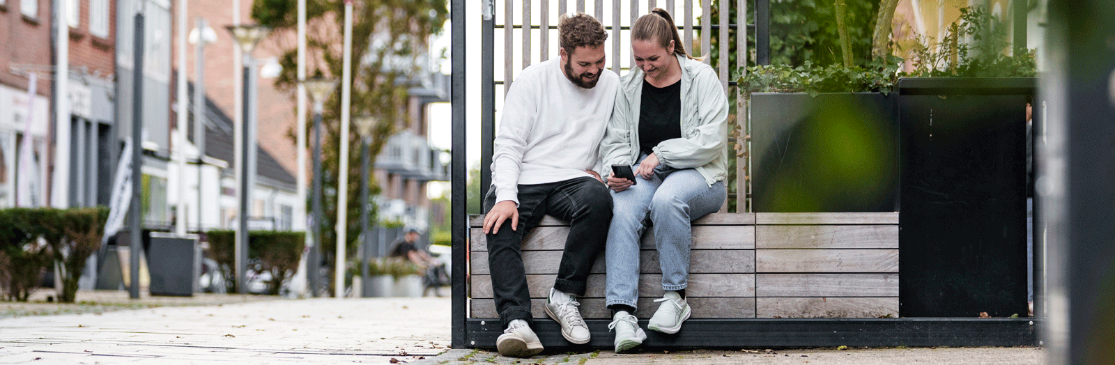 Par sidder og kigger på en telefon i en gågade