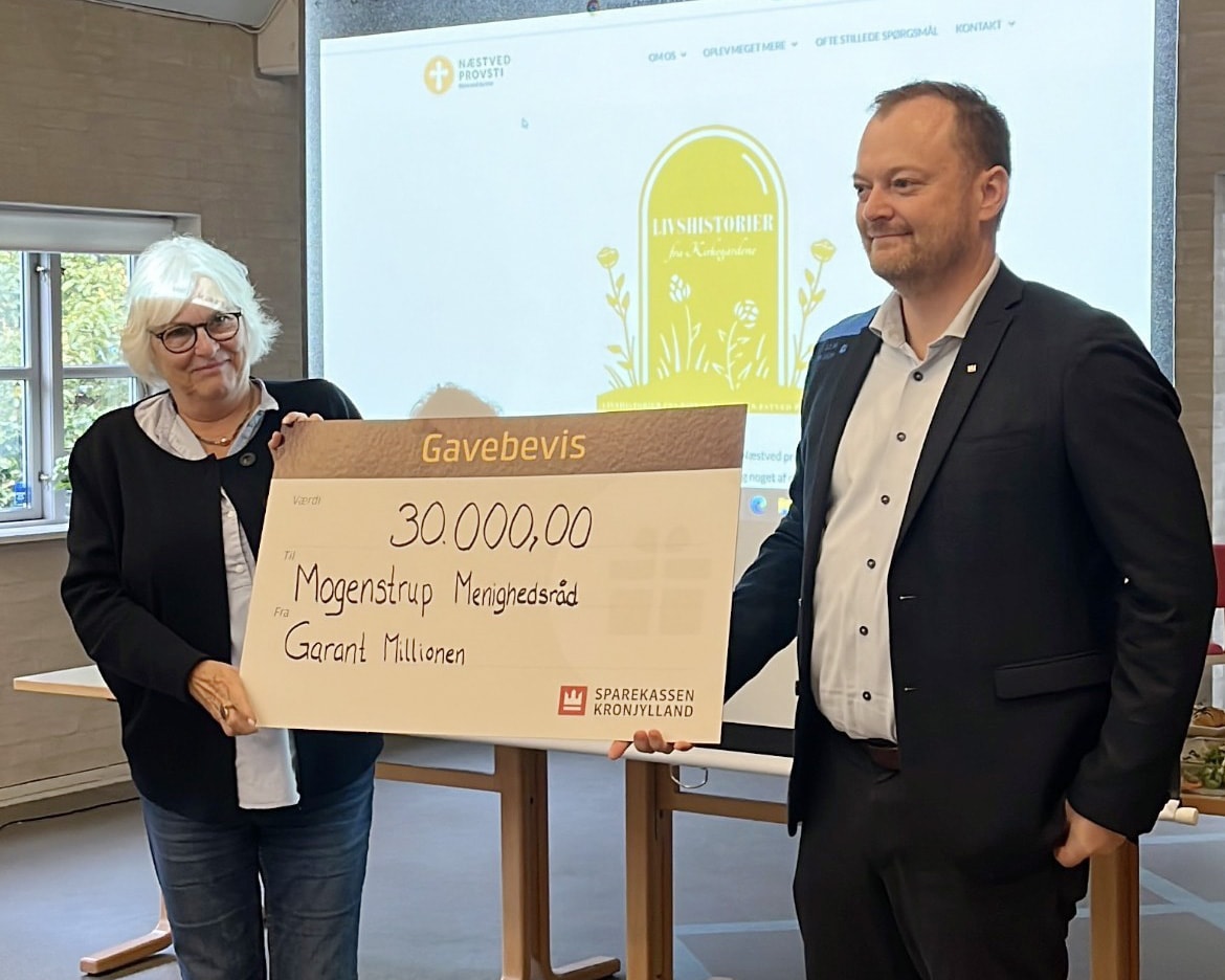 Erhvervskundechef Ulrik Hansen fra Sparekassen Kronjylland i Slagelse overrækker en donation til Næstelsø-Mogenstrup Menighedsråd til deres 'Fortællinger fra kirkegården'-projekt.