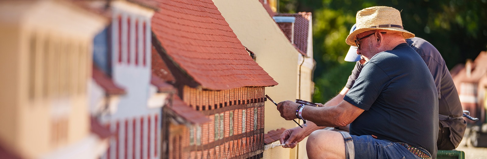 To mænd sidder og maler en miniatureudgave af et bindingsværkhus i Køge Miniby.