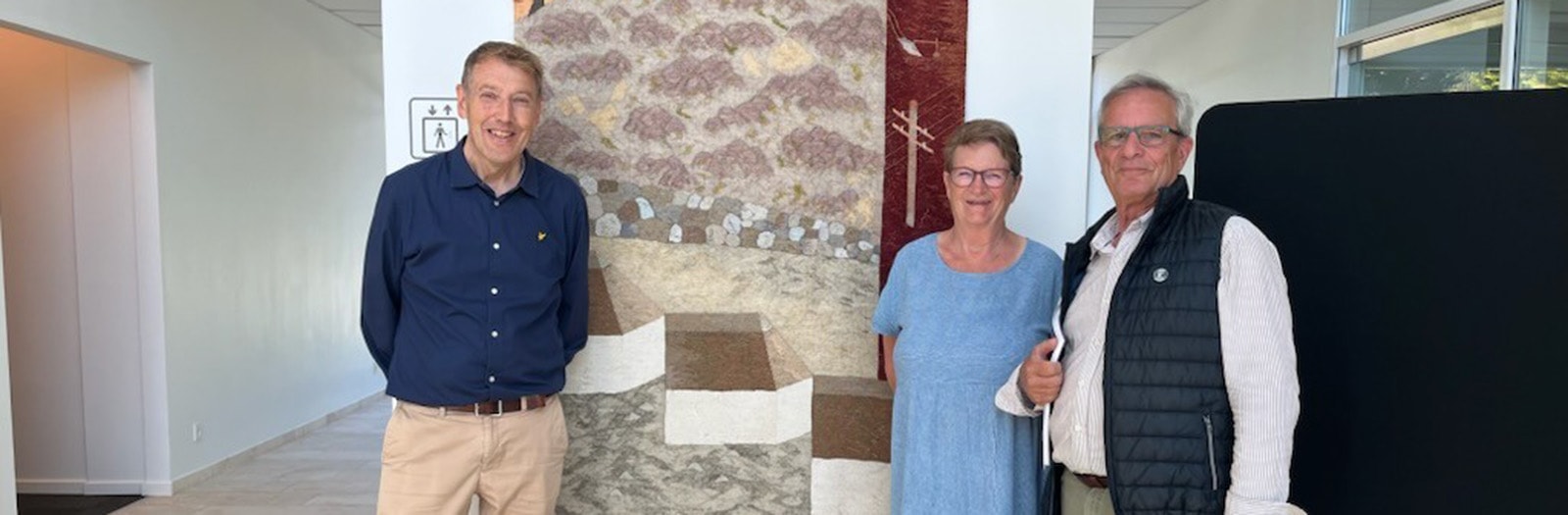 Jeremy Watts fra historiegruppen under Vorbasse Lokalråd, afdelingsdirektør H. C. Christensen fra Sparekassen Kronjylland og Inger Donslund fra frivilliggruppen under Vorbasse Bibliotek fotograferet foran vægtæppet i Sparekassen Kronjylland i Vorbasse.